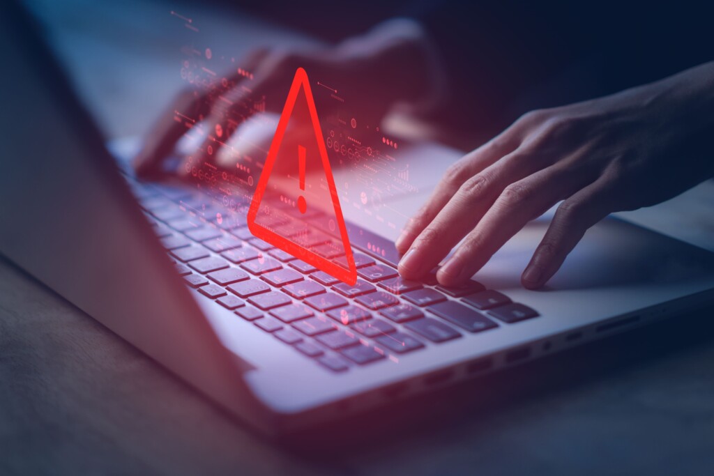Hands typing on a laptop keyboard with a red warning symbol displayed on the screen