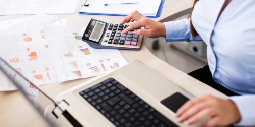 Professional calculating costs using a laptop and calculator with printed charts, representing managed IT service expenses in Central Ontario