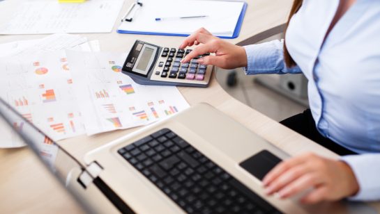 Professional calculating costs using a laptop and calculator with printed charts, representing managed IT service expenses in Central Ontario
