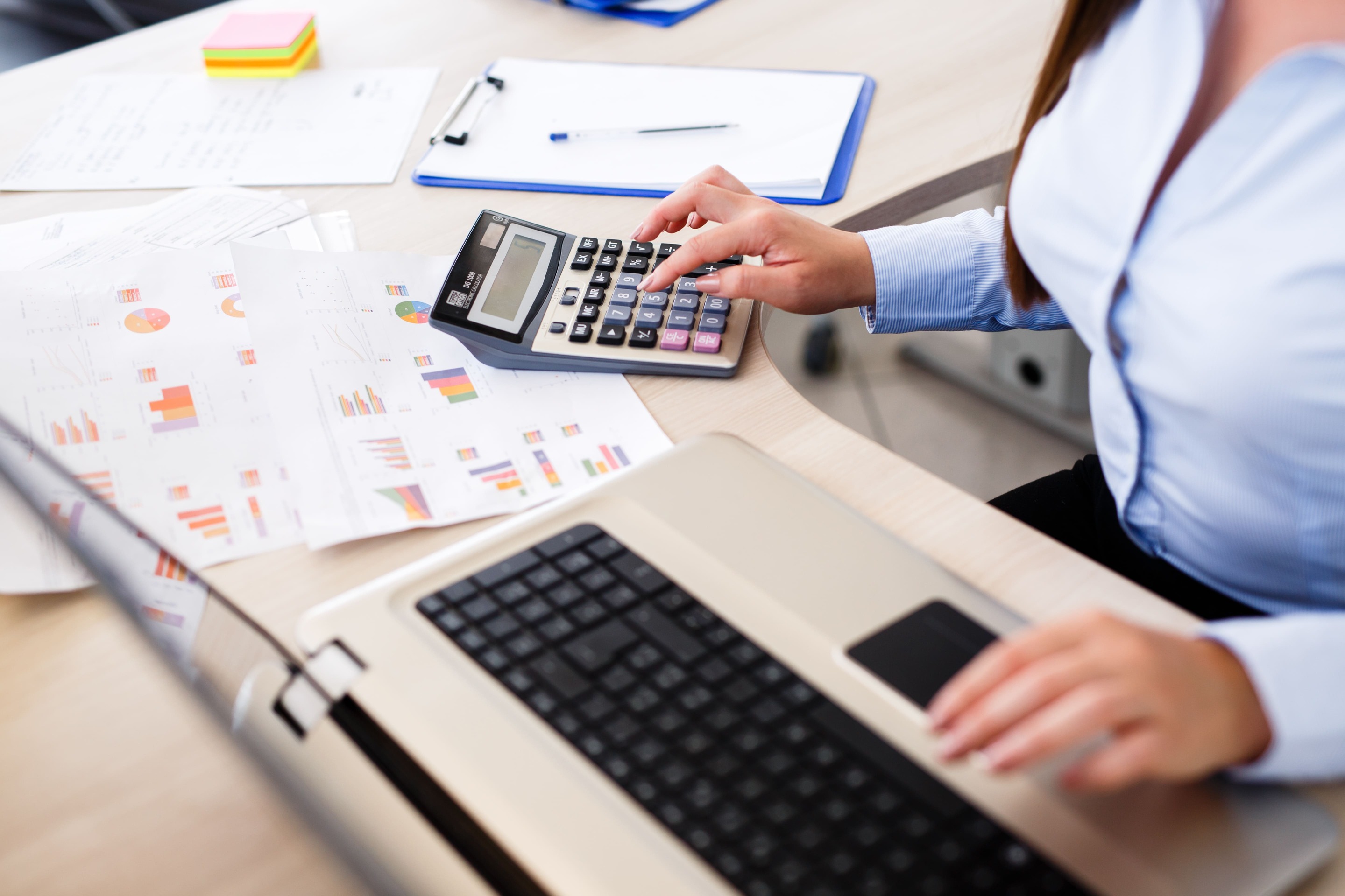 Professional calculating costs using a laptop and calculator with printed charts, representing managed IT service expenses in Central Ontario