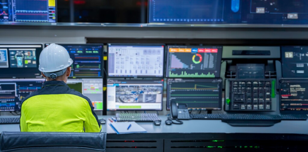 Engineer in a control room monitoring network systems on multiple screens, representing a network security audit with ACT360