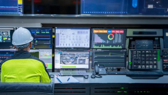 Engineer in a control room monitoring network systems on multiple screens, representing a network security audit with ACT360