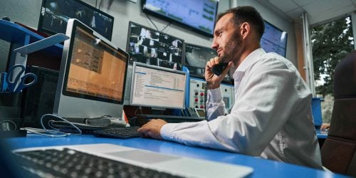 Man in a control room working on multiple computer monitors while talking on the phone
