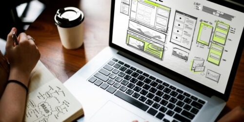 Laptop displaying HTML website wireframes on a desk with notes and a coffee cup, representing the web design process