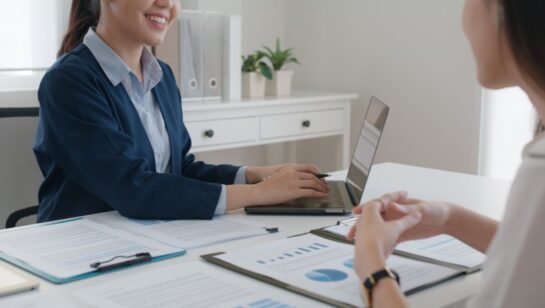 Business professional meeting with a client and reviewing documents on a laptop, representing the process of hiring IT consultants