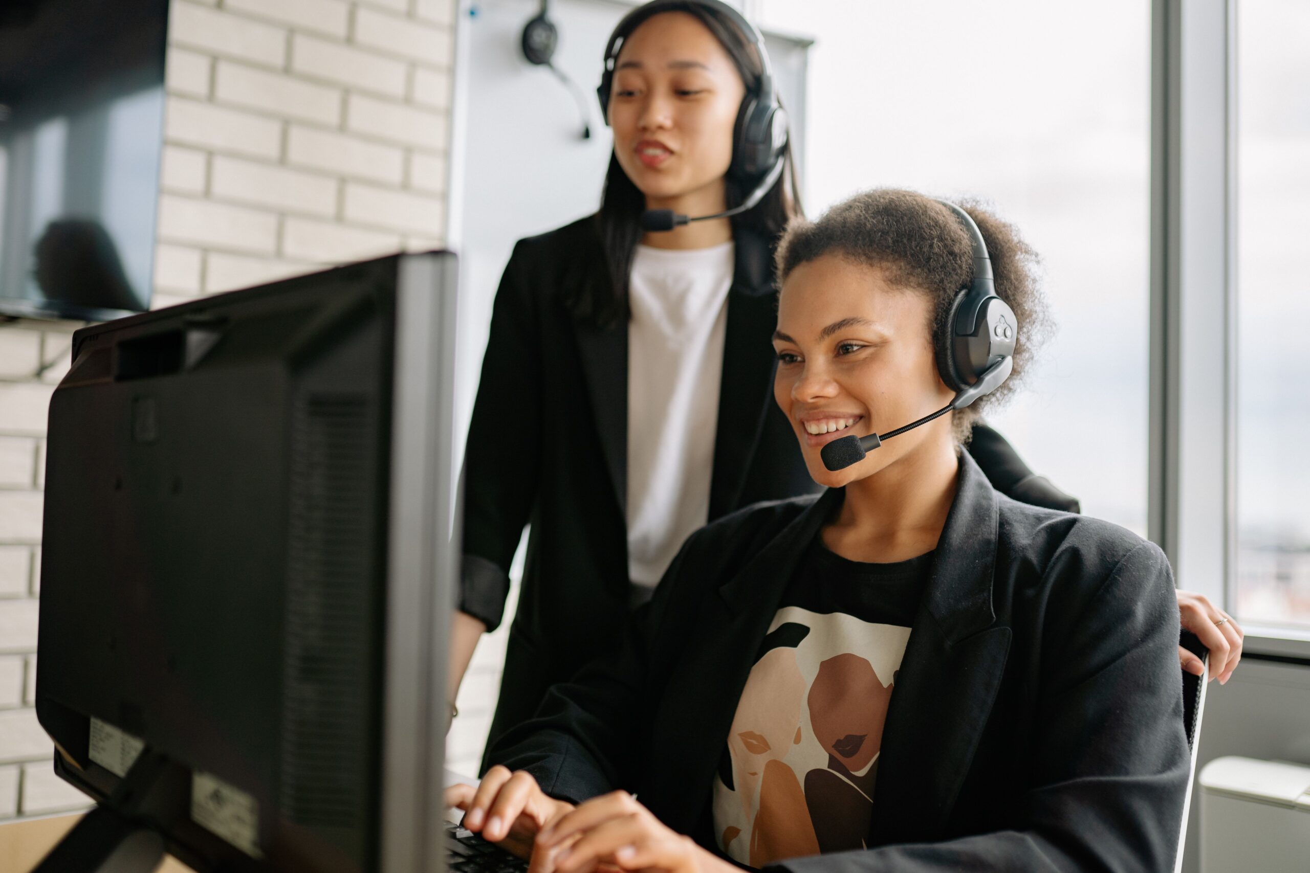 Two support professionals with headsets assisting a client at a computer in a bright office
