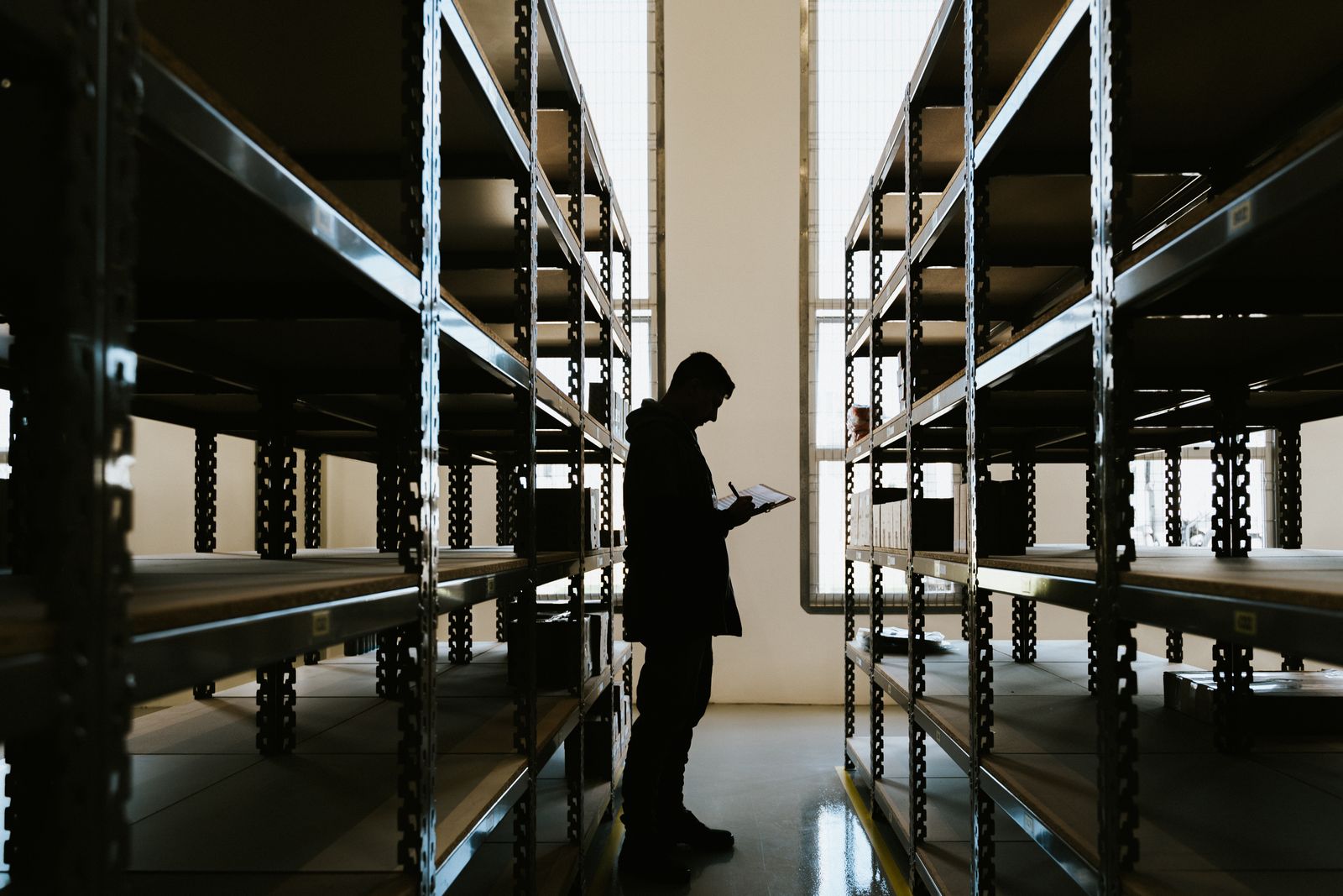 Silhouette of a person checking inventory on a clipboard in a warehouse aisle, representing an audit trail for inventory movement