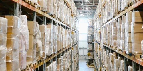 Warehouse aisle lined with shelves of parts and boxes, representing the truck and station level inventory a field service company needs to track