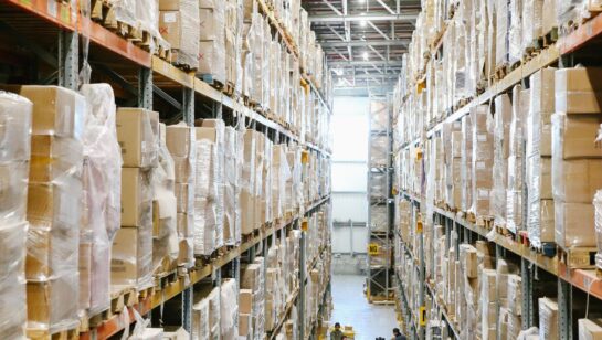 Warehouse aisle lined with shelves of parts and boxes, representing the truck and station level inventory a field service company needs to track