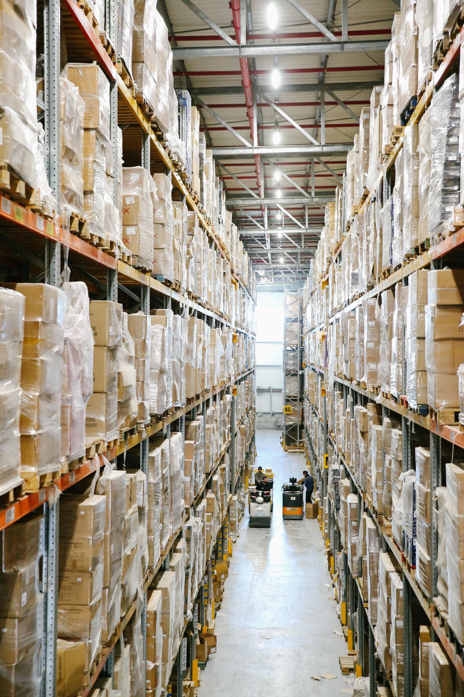 Warehouse aisle lined with shelves of parts and boxes, representing the truck and station level inventory a field service company needs to track