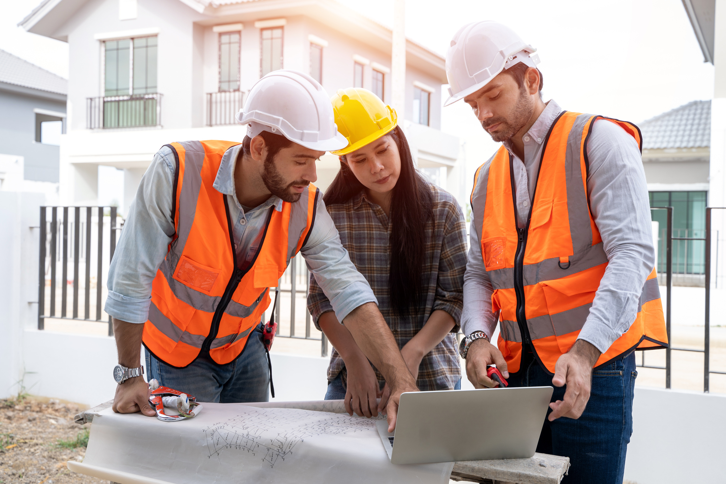 Construction project team reviewing blueprints and a laptop on site, the kind of quoting and scheduling work AI automation can speed up