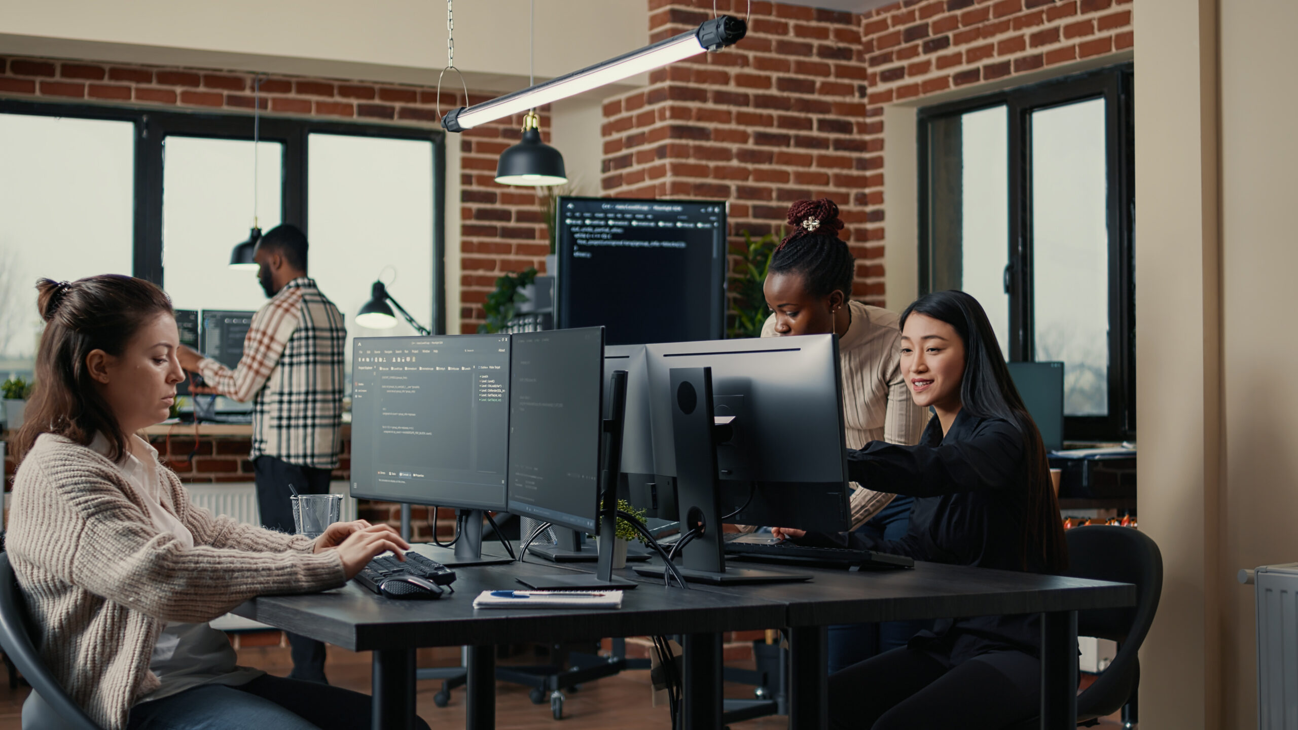 Software engineer typing code while colleagues work at a shared desk, the kind of technology team common in Markham
