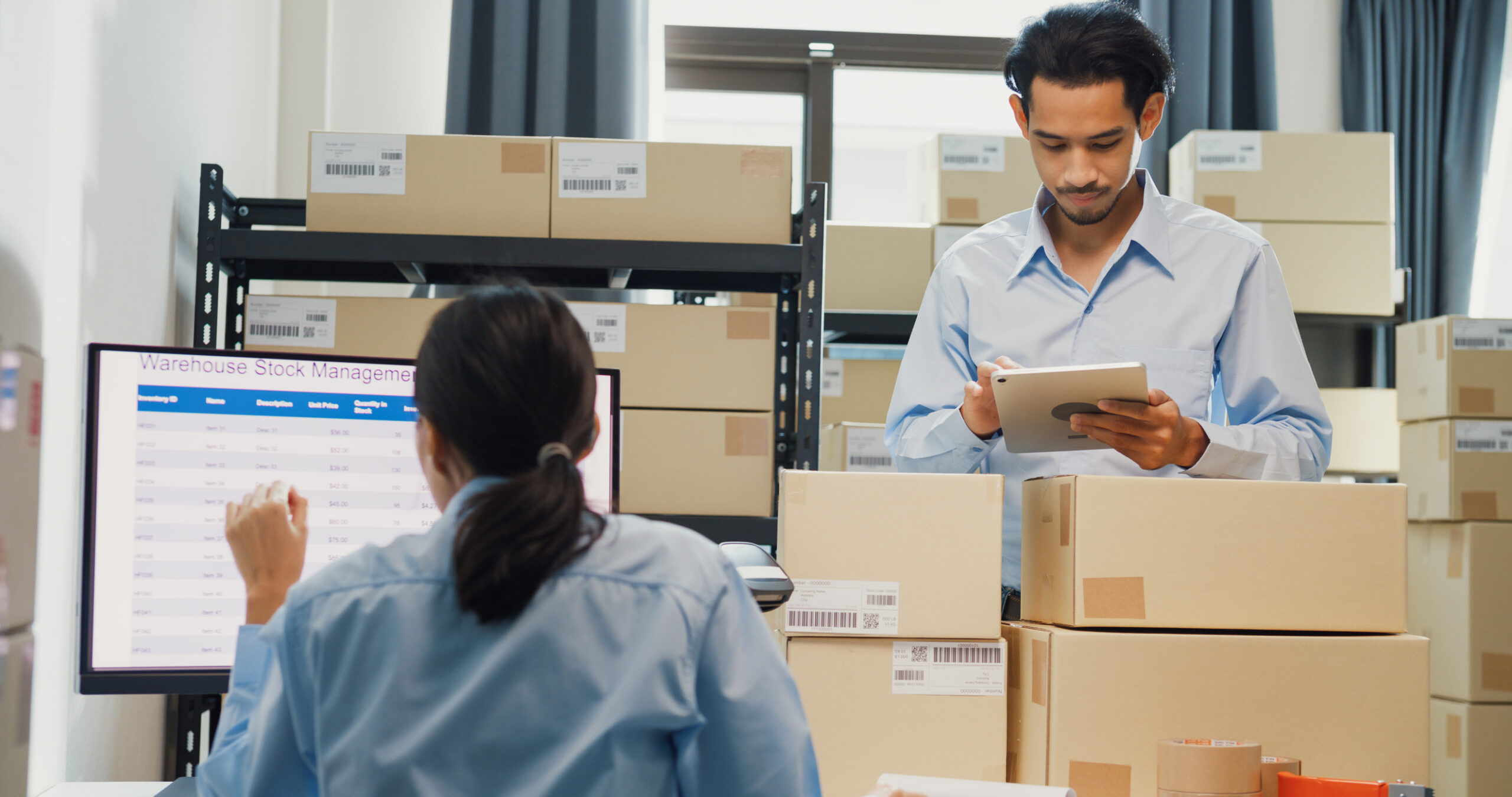 Warehouse team reviewing inventory data on a computer and tablet at a logistics desk