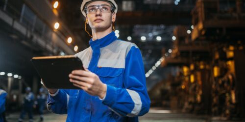 Manufacturing engineer using a tablet on the shop floor to track AI-driven production data and ROI
