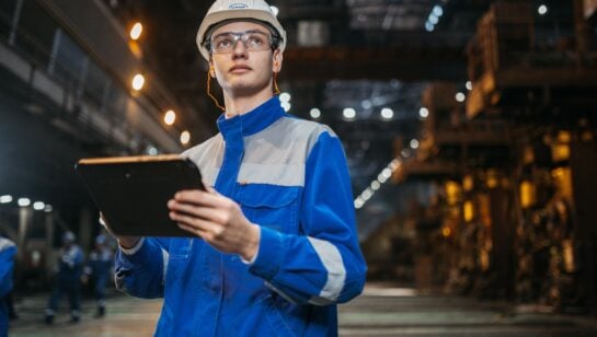 Manufacturing engineer using a tablet on the shop floor to track AI-driven production data and ROI
