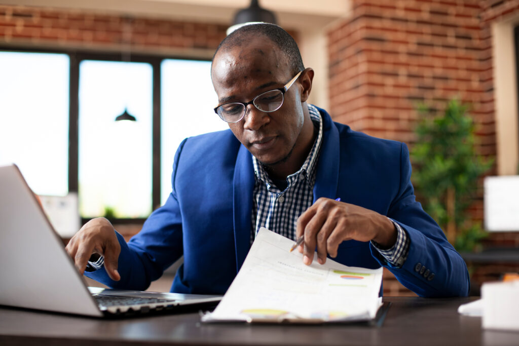 An analyst reviewing a checklist on a clipboard while working on a laptop, representing the planning process for a cloud migration