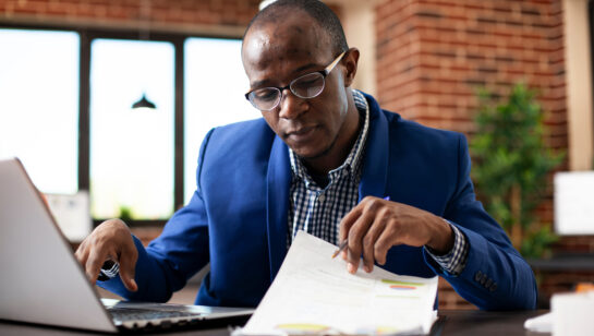 An analyst reviewing a checklist on a clipboard while working on a laptop, representing the planning process for a cloud migration