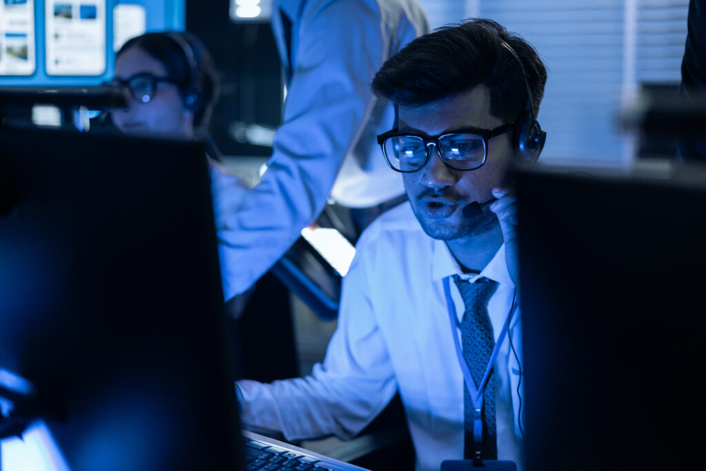 A cybersecurity analyst wearing a headset working in a security operations center, monitoring systems for threats