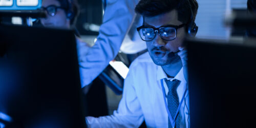 A cybersecurity analyst wearing a headset working in a security operations center, monitoring systems for threats