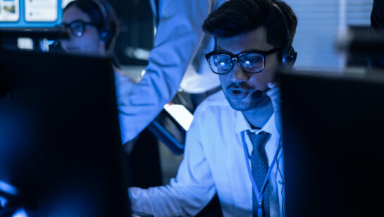 A cybersecurity analyst wearing a headset working in a security operations center, monitoring systems for threats
