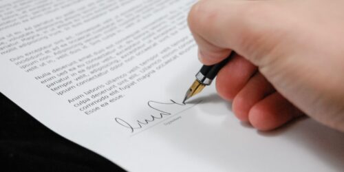 Close-up of a hand signing a document with a pen, representing signing off on a cyber insurance policy application