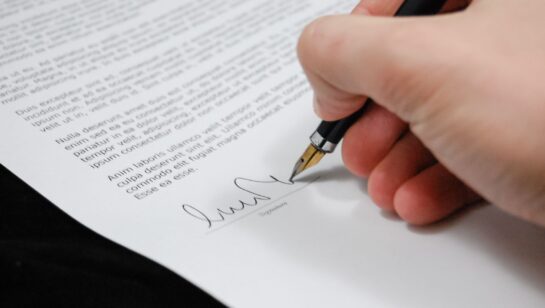 Close-up of a hand signing a document with a pen, representing signing off on a cyber insurance policy application