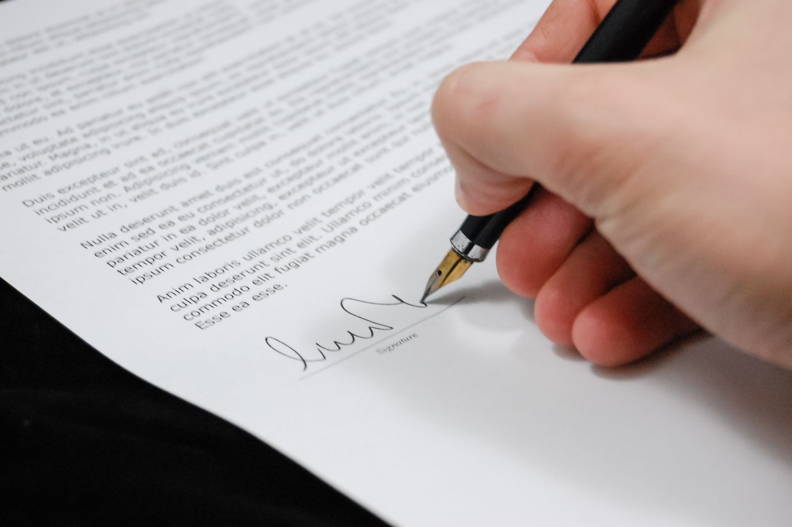 Close-up of a hand signing a document with a pen, representing signing off on a cyber insurance policy application