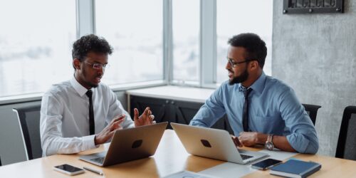 Two colleagues discussing which AI tool fits a specific business task on a laptop