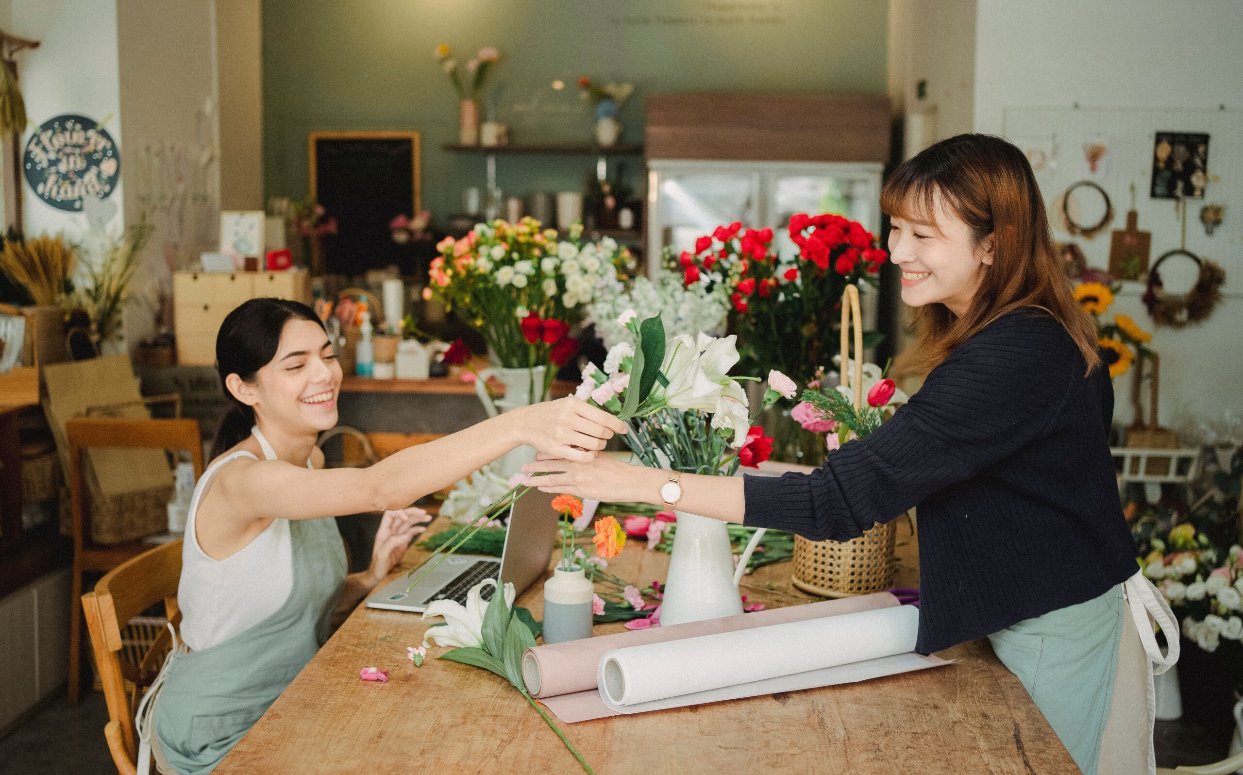 Two small business owners in aprons working together at a laptop in their retail shop