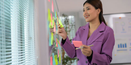 Manager arranging sticky notes on an office whiteboard during a team meeting to map a workflow before automating it