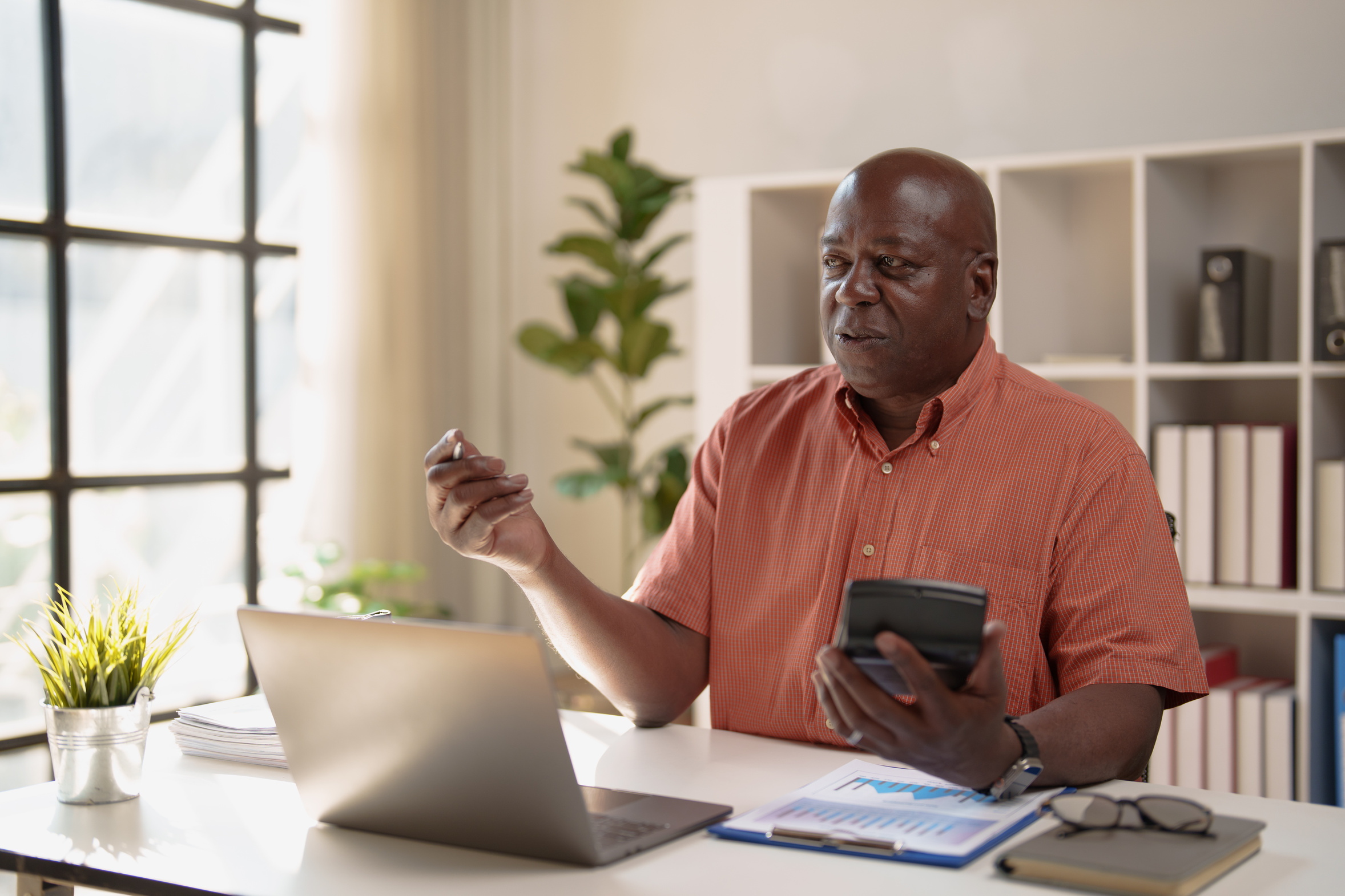 Aurora business owner working through monthly costs with a calculator and laptop at his office desk
