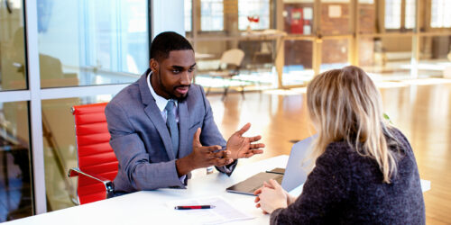 Business owner questioning a managed IT provider across a meeting table, with a written proposal between them