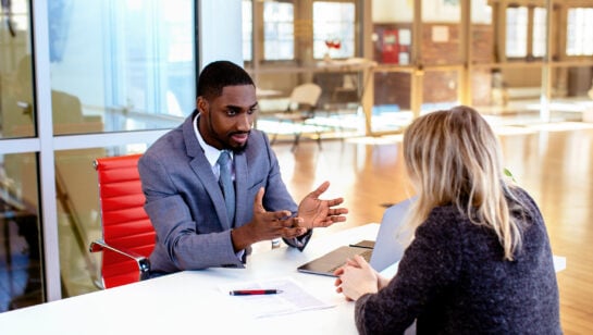 Business owner questioning a managed IT provider across a meeting table, with a written proposal between them