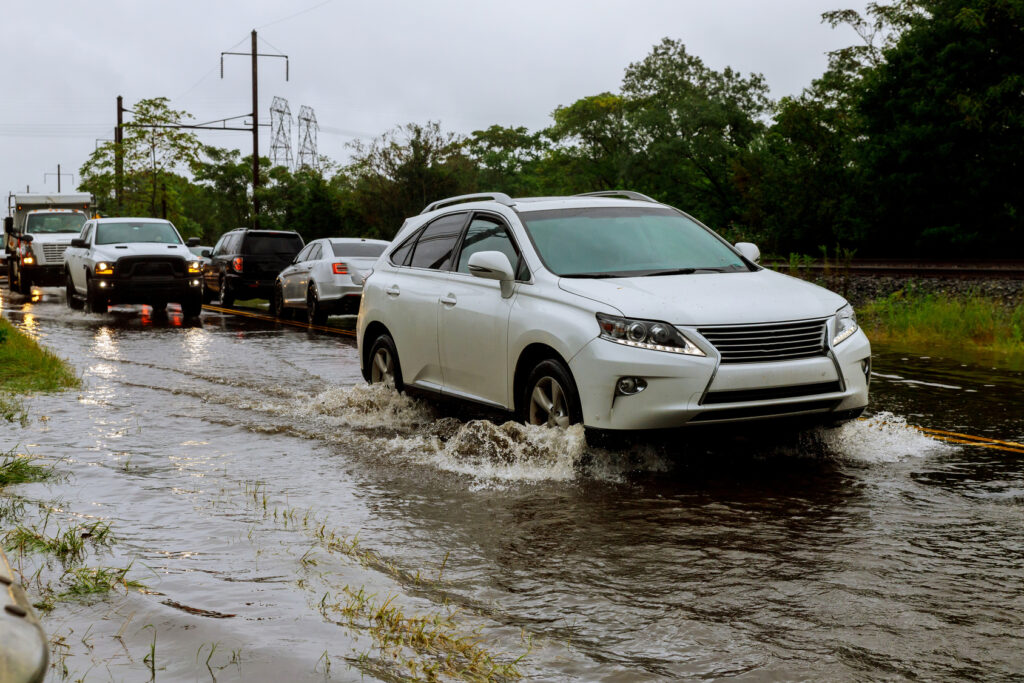 Cars driving through a flooded road during heavy rain, the kind of disruption that stops deliveries and staff from reaching work