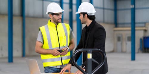 Warehouse manager and staff member reviewing systems on a laptop in a distribution centre, the kind of operation where an in-house IT lead works with an outside team