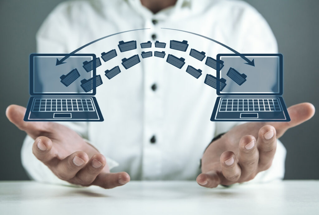 Two laptops side by side with files moving between them, representing the data and system handover when a business switches IT providers