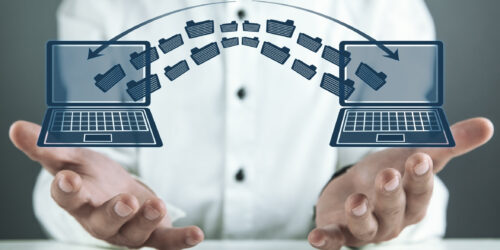 Two laptops side by side with files moving between them, representing the data and system handover when a business switches IT providers