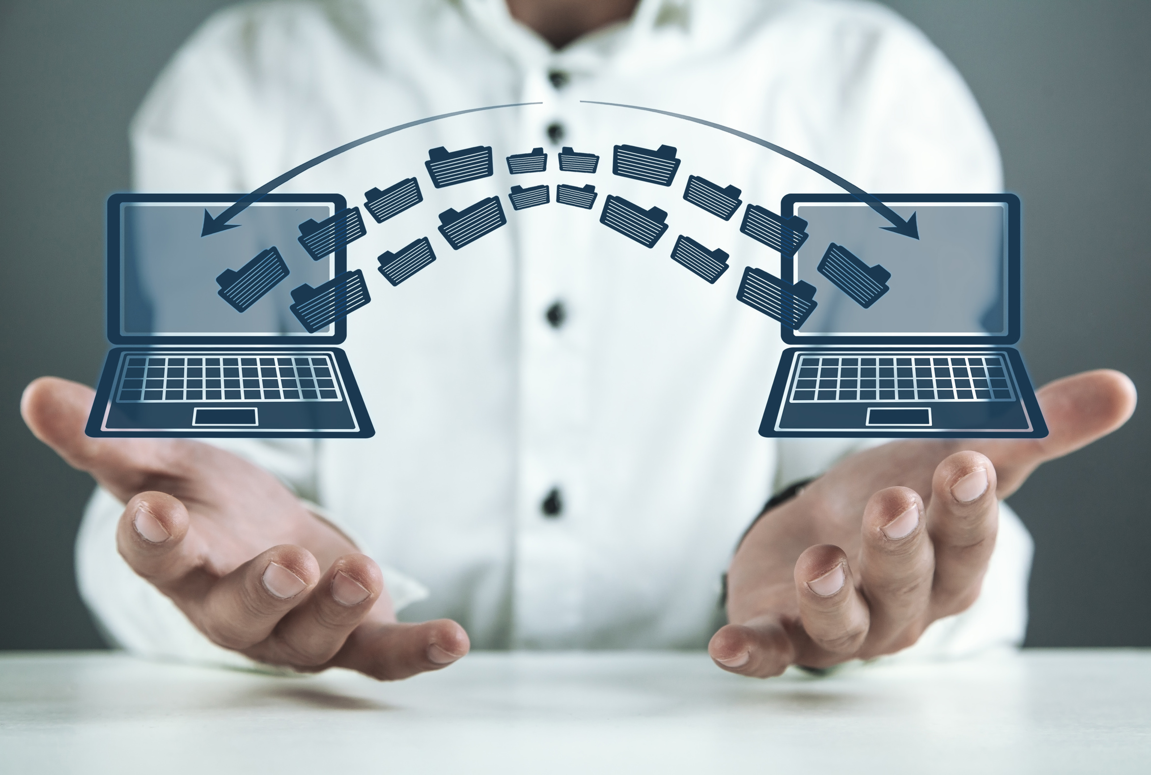 Two laptops side by side with files moving between them, representing the data and system handover when a business switches IT providers