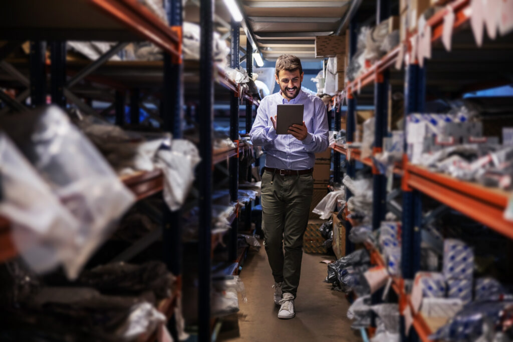 Warehouse supervisor walking the storage aisles and checking stock on a tablet