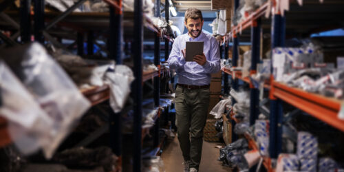 Warehouse supervisor walking the storage aisles and checking stock on a tablet