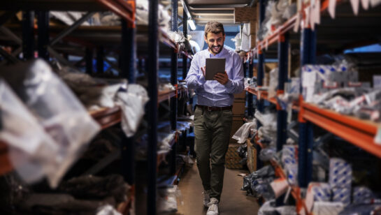 Warehouse supervisor walking the storage aisles and checking stock on a tablet