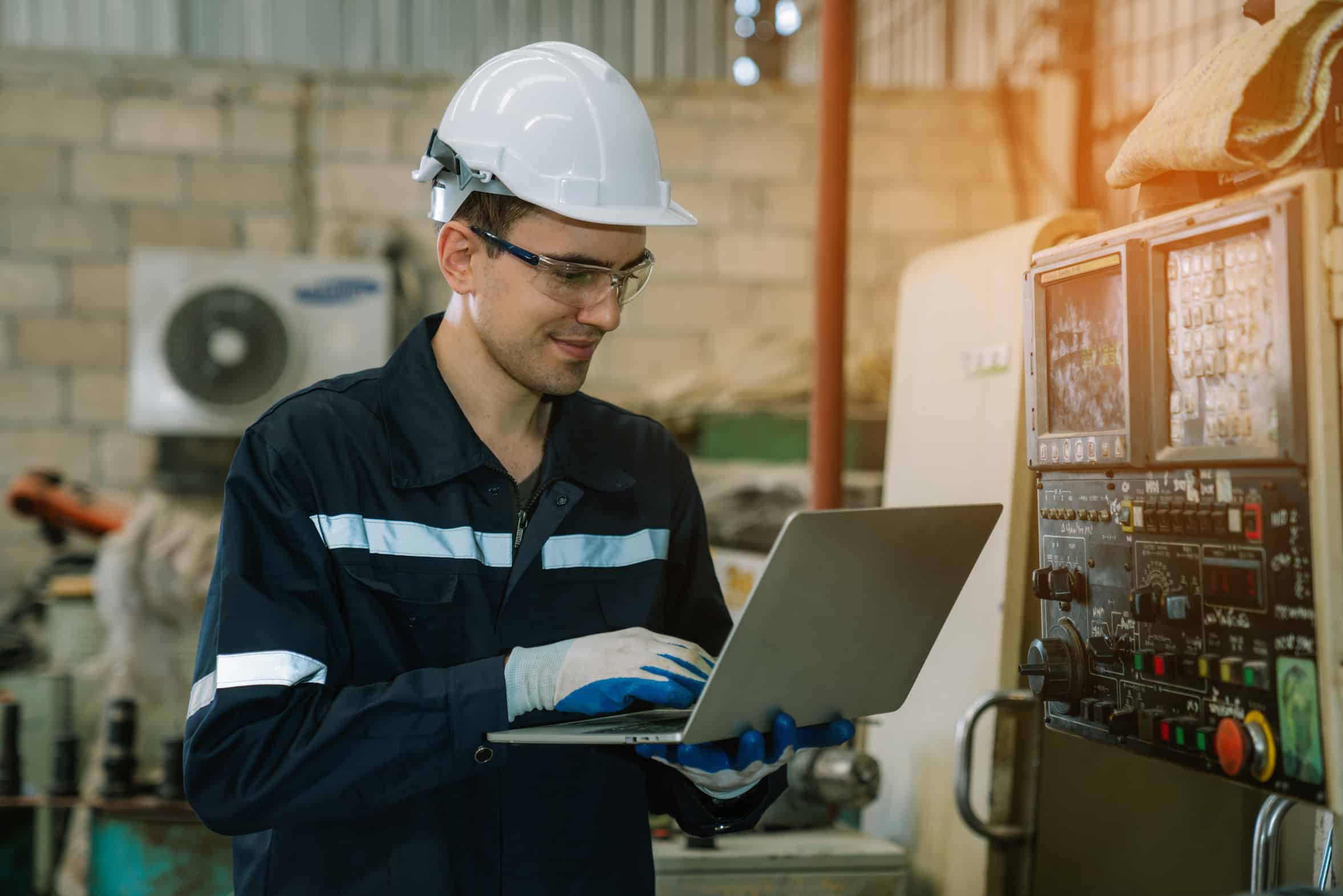 Engineers using a laptop to check a metal pressing machine on a plant floor, the production equipment a manufacturer's IT budget has to protect