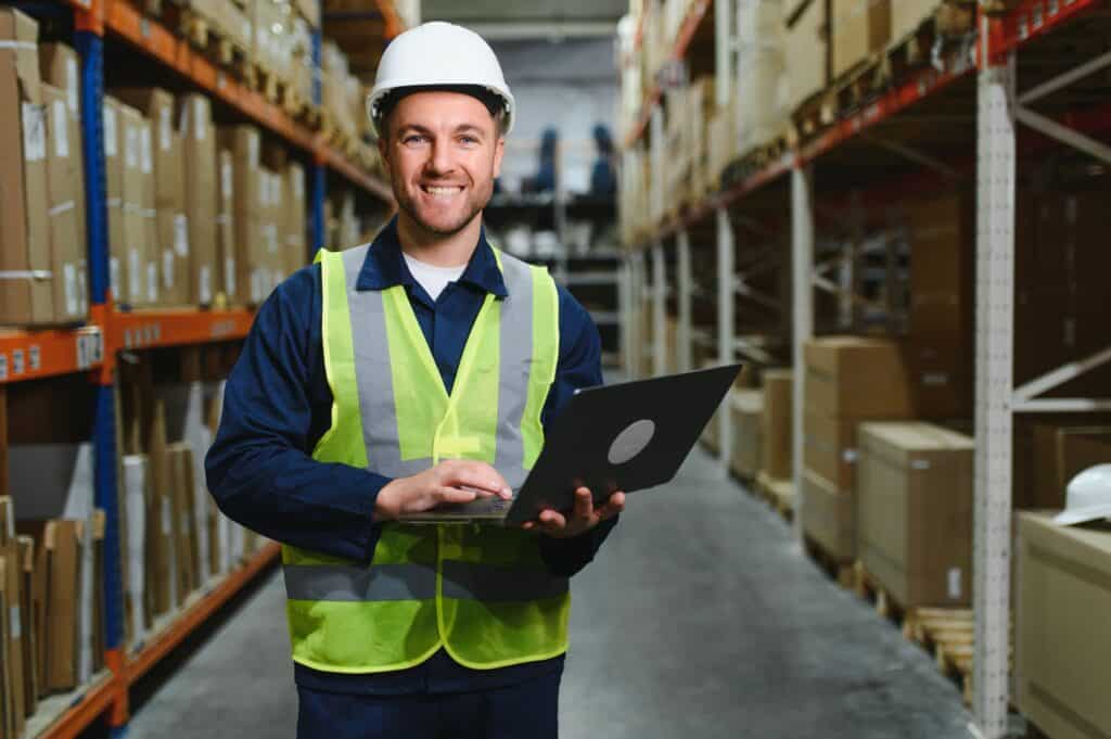 Warehouse worker checking incoming stock on a laptop beside shelving, the kind of system a Vaughan distributor needs running every shift