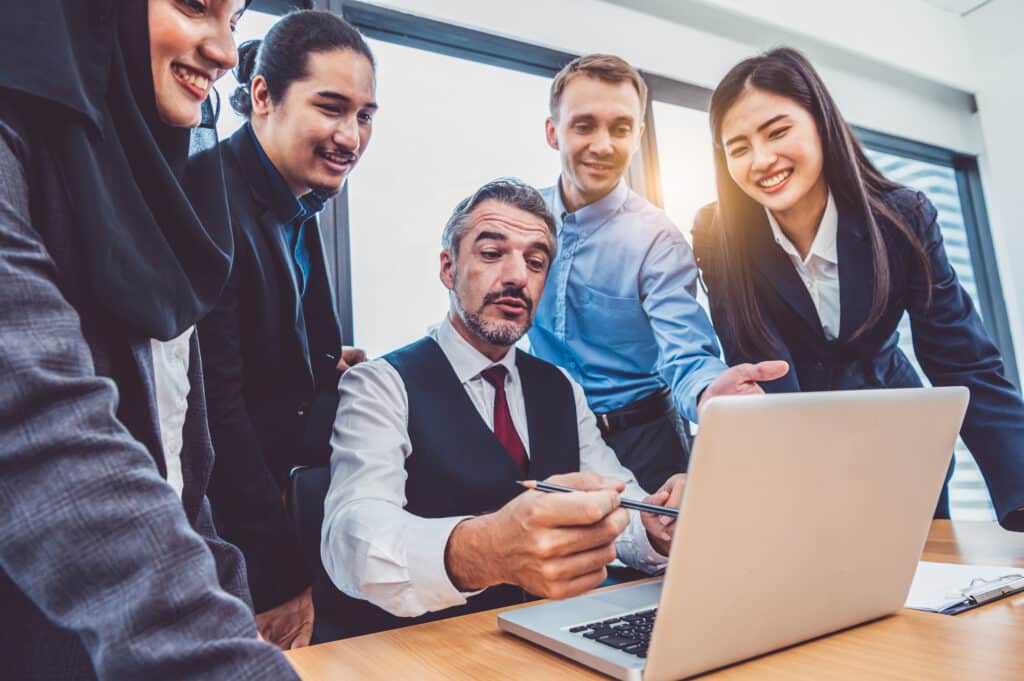 Business owner walking a growing team through a new process on a laptop in a modern office