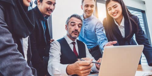 Business owner walking a growing team through a new process on a laptop in a modern office