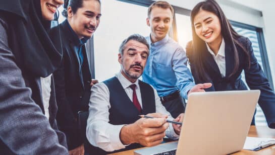 Business owner walking a growing team through a new process on a laptop in a modern office