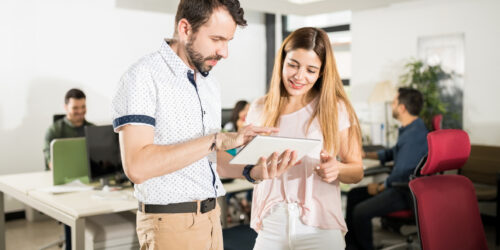 Experienced colleague helping a new employee at her computer, the kind of desk-side help a growing office relies on