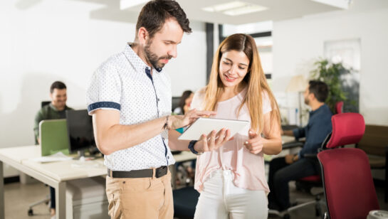 Experienced colleague helping a new employee at her computer, the kind of desk-side help a growing office relies on
