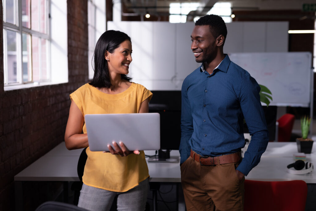 Two colleagues standing in an office looking at a laptop together, like an IT contact who already knows the team working through an issue with a staff member