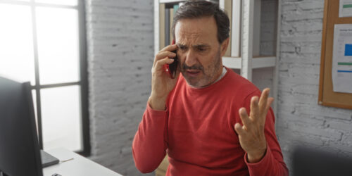 Frustrated business owner on the phone at his office desk, chasing his IT provider about a computer problem